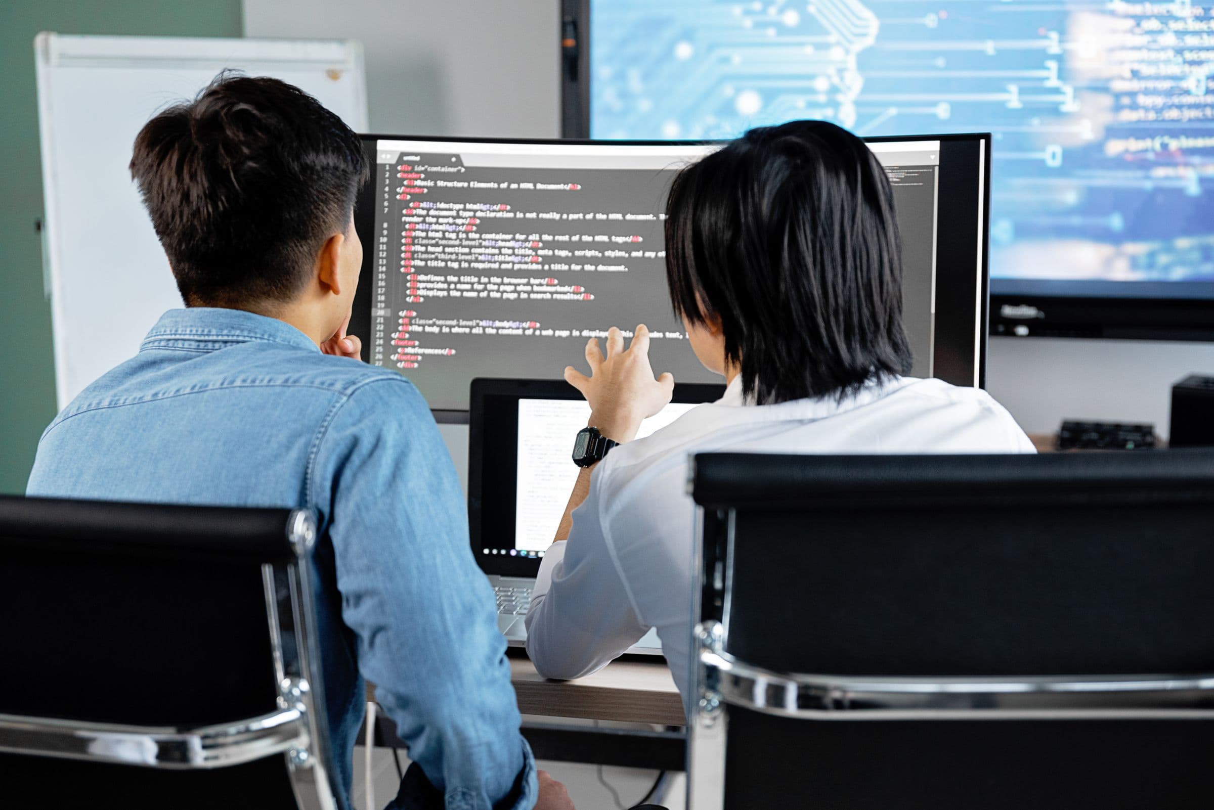 Two software developers reviewing code together on a monitor in a modern office